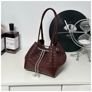 Detail of dark brown woven bucket bag featuring silver chain and pearl pendant decoration