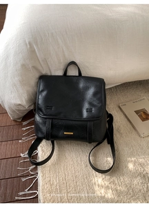 Minimalist black vintage leather backpack with gold metal logo in an aesthetic home setting