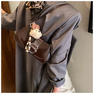 Détail du sac baguette en cuir marron brillant avec boucle argentée et breloque ours
