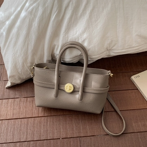 Detail of taupe pebbled leather handbag with gold circular twist-lock closure on wooden floor
