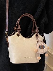 Cream bucket bag with dark brown handles and sheep pendant shown on a black wool coat