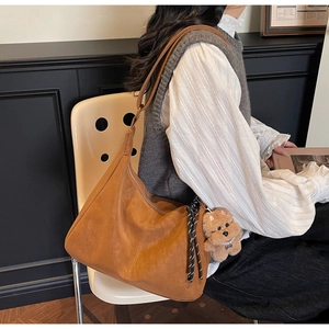 Detailed side view of brown suede tote bag with cute bear charm and woven cord detail