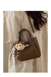 Detail of dark brown lychee grain leather bucket bag with silver lock and plush bear charm