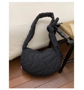 Detail of wave quilted black crossbody bag with knot wide strap on a woven chair