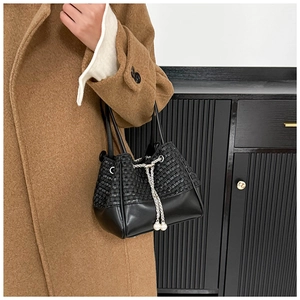 Detailed view of black woven bucket bag with pearl drawstring and metal chain accent