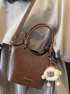 Brown leather bucket bag with knot handle, gold hardware and plush sheep charm decoration