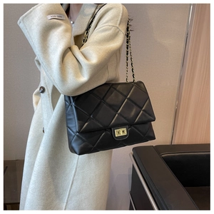 Détail d'un sac à bandoulière en cuir matelassé noir avec chaîne dorée sur manteau
