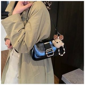 Détail du sac à bandoulière noir brillant avec boucle et breloque ours en peluche