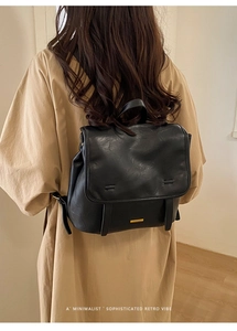 Minimalist black leather backpack shown on model with vintage flip-top and metal plate