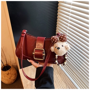 Détail d'un sac bandoulière en cuir verni rouge avec boucle dorée et breloque en peluche