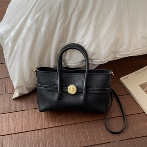 Detail of black pebbled leather handbag with golden round twist lock and handle