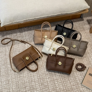 Flat lay of litchi grain leather tote bags in five earthy tones with golden twist locks