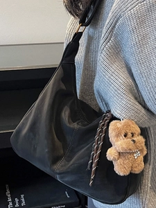 Minimalist black tote bag with plush bear charm and metallic ring detail on shoulder strap
