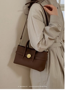 Detail of retro brown leather handbag with gold twist lock on a beige skirt outfit