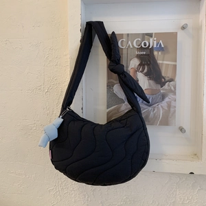 Detail of black quilted crescent bag featuring knotted strap and cute plush charm