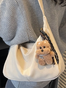 Minimalist beige pleated tote bag with plush dog charm worn by a model in a casual style