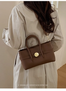 Brown lychee grain leather handbag with gold metal lock buckle on a long beige coat