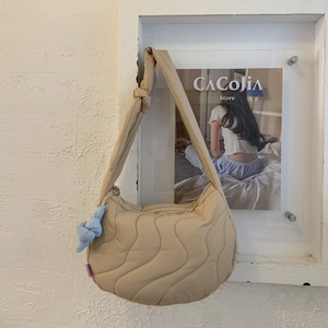 Close-up of beige quilted moon bag with wavy stitching and blue knot accessory