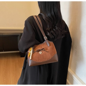 Close-up of vintage brown suede shoulder bag with bow detail and beaded charm