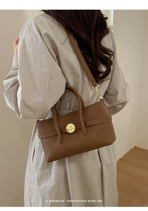 Close-up of brown pebbled leather bag with a golden circular twist lock and handle