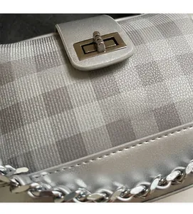 Detail shot of silver checkerboard textured fabric and metal twist-lock on a shoulder bag