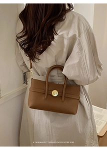 Close-up of brown pebbled leather texture with a gold circular clasp on a retro bag