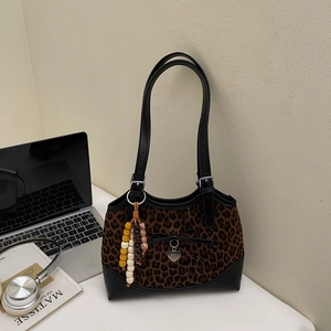 Detailed view of leopard print shoulder bag with black bow and heart pendant on a desk