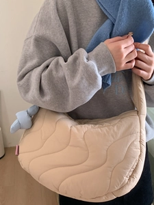 Quilted beige crescent crossbody bag for women with wave stitching and plush pendant