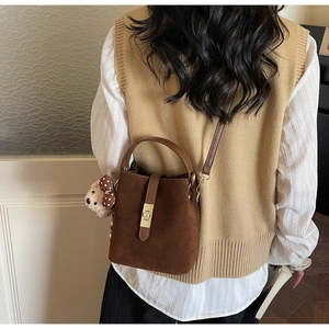 Detail of dark brown suede bucket bag with teddy bear charm worn with a vest