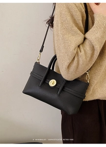 Detail shot of black litchi grain leather bag with gold buckle on a model wearing beige