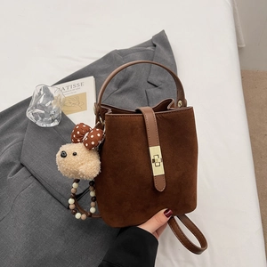 Detail of retro brown suede bucket bag with gold metal lock and cute plush bear charm