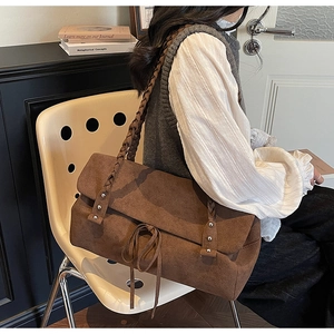Dettaglio di una borsa tote in pelle scamosciata marrone con tracolla intrecciata e rivetti