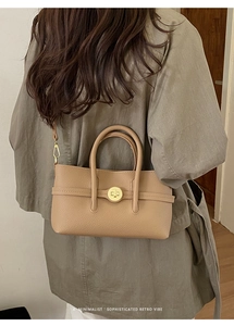 Close-up of beige lychee grain leather crossbody bag with golden metal buckle details