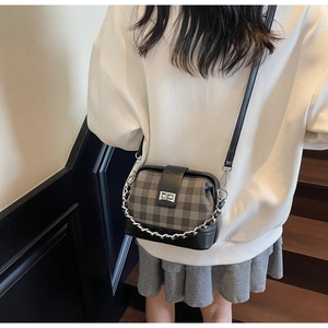 Detailed view of grey plaid crossbody bag with silver chain worn by a model in casual outfit