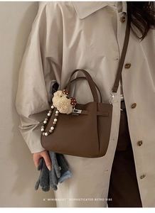 Close-up of retro dark brown lychee leather bucket bag with bear charm and buckle