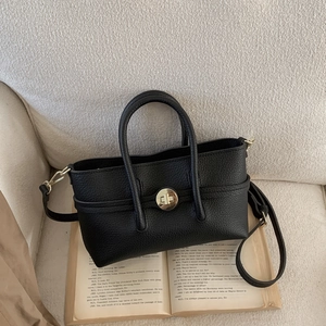 Detail of black lychee grain leather handbag with gold twist lock on a book background