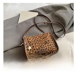 Close-up of leopard print crossbody bag with brown leather trim and golden star pendant