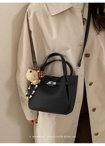 Detail of black pebbled leather bucket bag with metal turn-lock and cute bear pendant