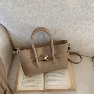 Detail of khaki lychee grain leather handbag with gold rotary lock on an open book