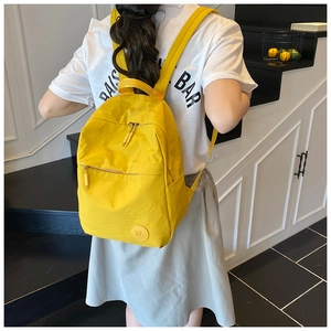 Vue détaillée d'un sac à dos en nylon jaune vif léger avec un écusson logo M rond
