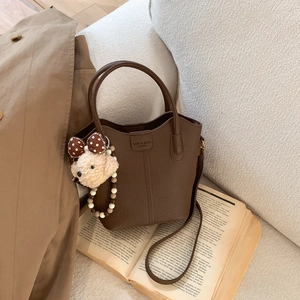 Detail der dunkelbraunen Eimer-Tasche aus Leder mit Bärenanhänger auf Buch