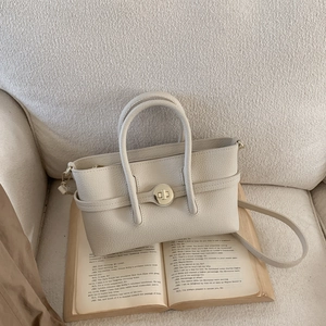 Detail view of cream leather crossbody bag with metal twist lock on a vintage book