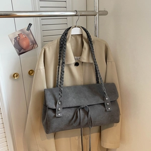 Detail of grey suede shoulder bag featuring a braided strap and silver rivet accents