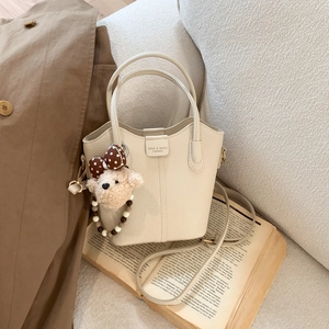 Detail der cremeweißen Beuteltasche mit Litschi-Textur und braunem Plüschbär-Anhänger
