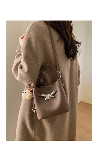 Close-up of brown lychee grain leather bucket bag with silver buckle and plush bear charm