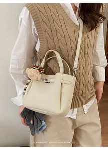 Chic off-white bucket bag with a cute bear charm shown worn by a model in a retro style