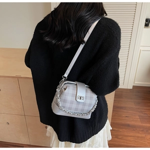 Silver checkered crossbody bag with chain detail worn over a black knit sweater