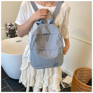 Gros plan du sac à dos en nylon bleu clair avec logo M et bretelles porté par un modèle