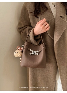 Brown litchi leather bucket bag with metal buckle and teddy bear charm on model arm