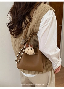 Chic caramel bucket bag with lychee grain leather and plush dog charm on a model